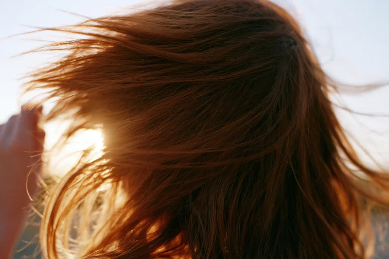 Woman tossing long auburn hair in wind with sunlight behind her