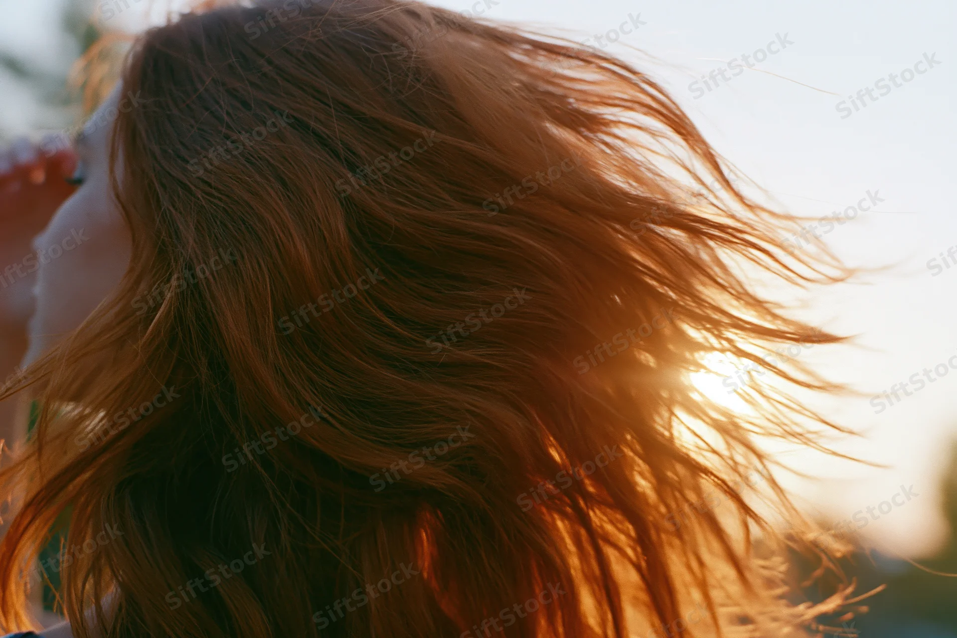 Woman with long auburn hair flowing in wind backlit by sunlight outdoors