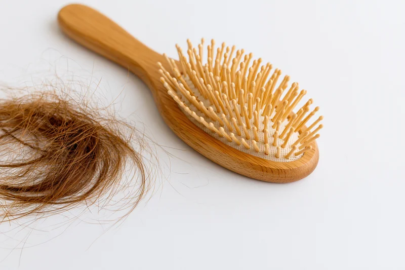 Wooden hairbrush with shed hair on white surface