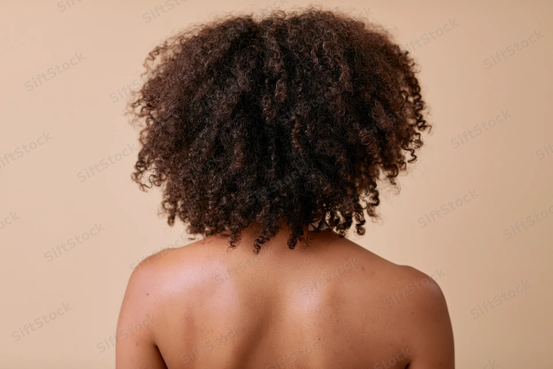 Back view of a black woman with natural curly afro hair, bare shoulders, studio portrait