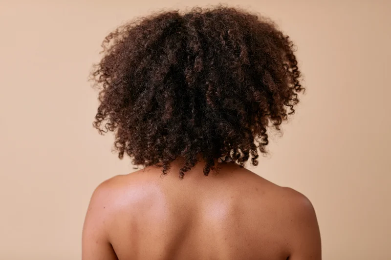 Back view of a black woman with natural curly afro hair, bare shoulders, studio portrait