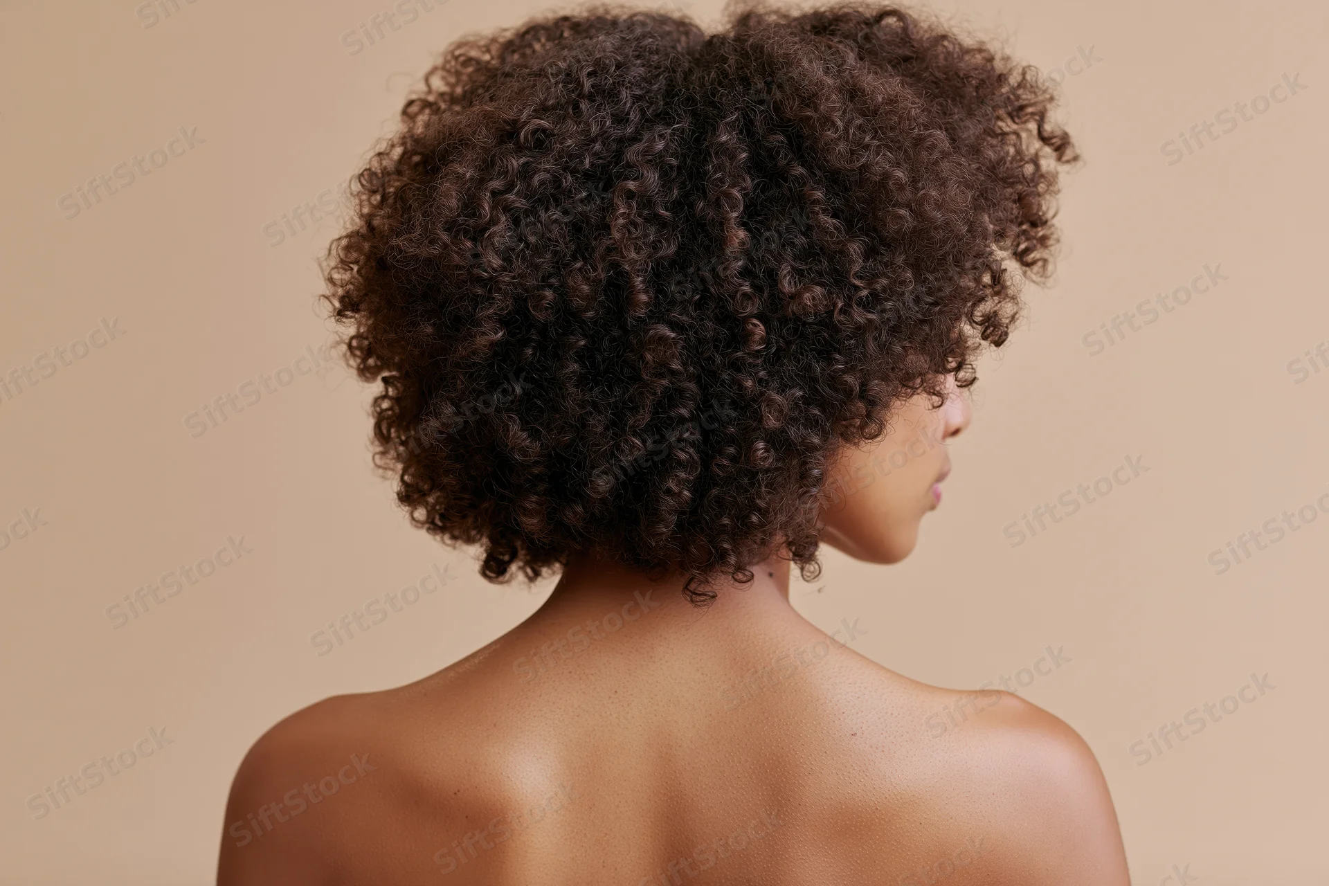 Young black woman with natural curly afro hair seen from back bare shoulders in studio setting