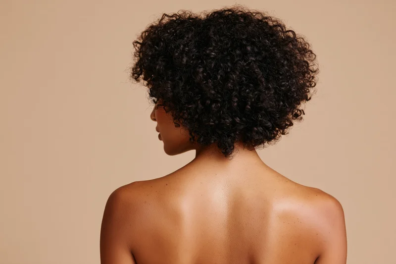 Black woman with curly natural afro hair shown from back bare shoulders in studio setting