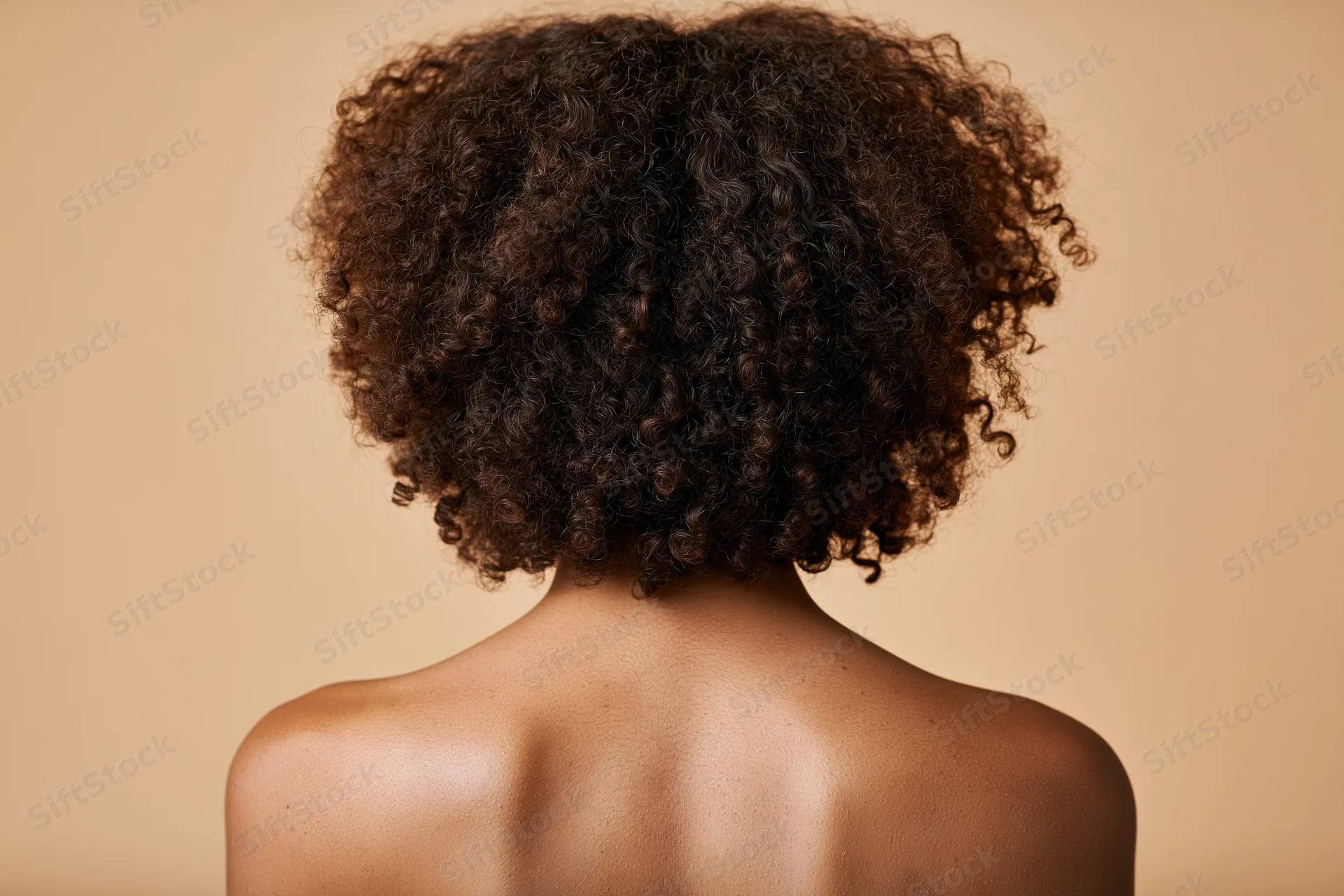 Back view of a black woman with natural curly hair showing bare shoulders against a neutral background