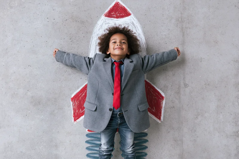 Child in oversized blazer standing on spring with chalk rocket drawn behind them on concrete wall