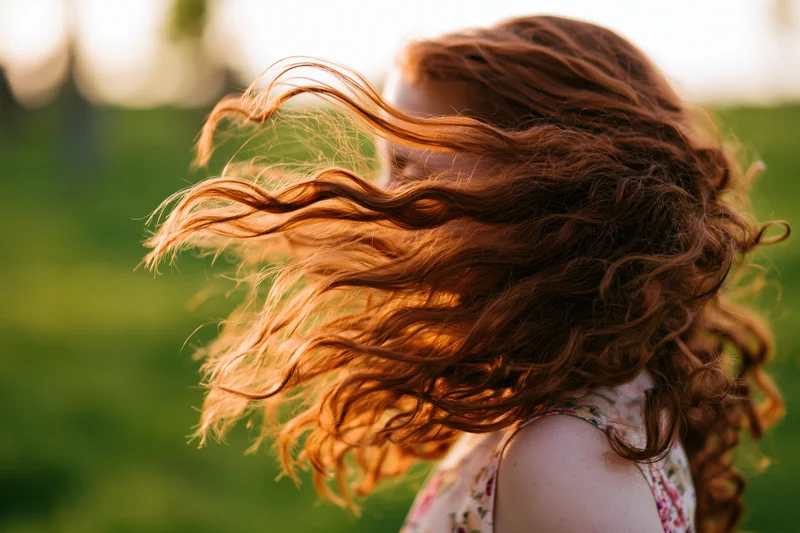 Girl spinning outdoors with long curly auburn hair flying in the wind