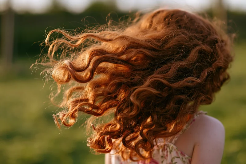 Young girl spinning outdoors with long curly auburn hair flying in the wind