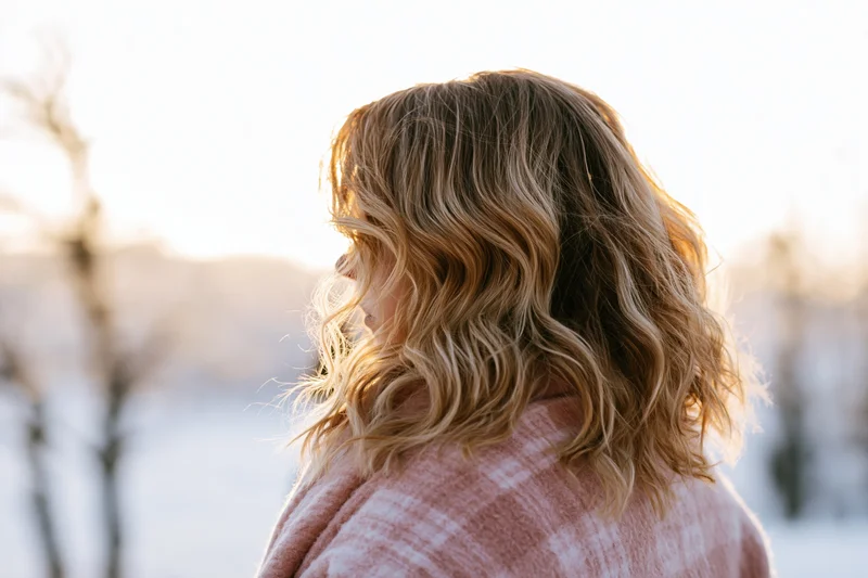 Woman with wavy blonde hair seen from behind in snowy landscape at sunset