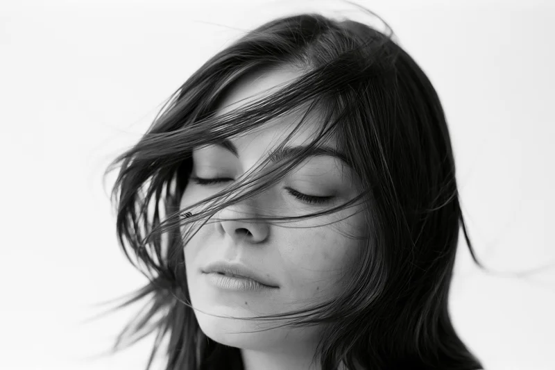 Closeup portrait of a woman with long dark hair flowing across her face against a white background