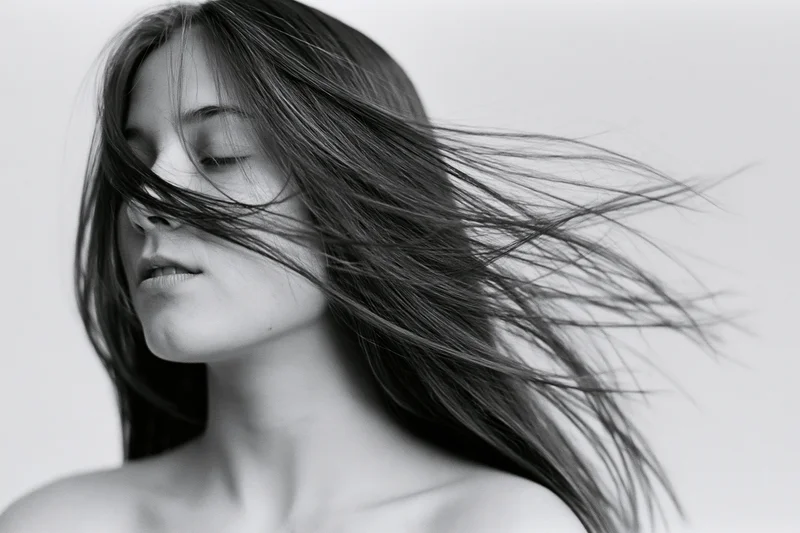 Woman with long straight hair flowing in wind, eyes closed, studio portrait