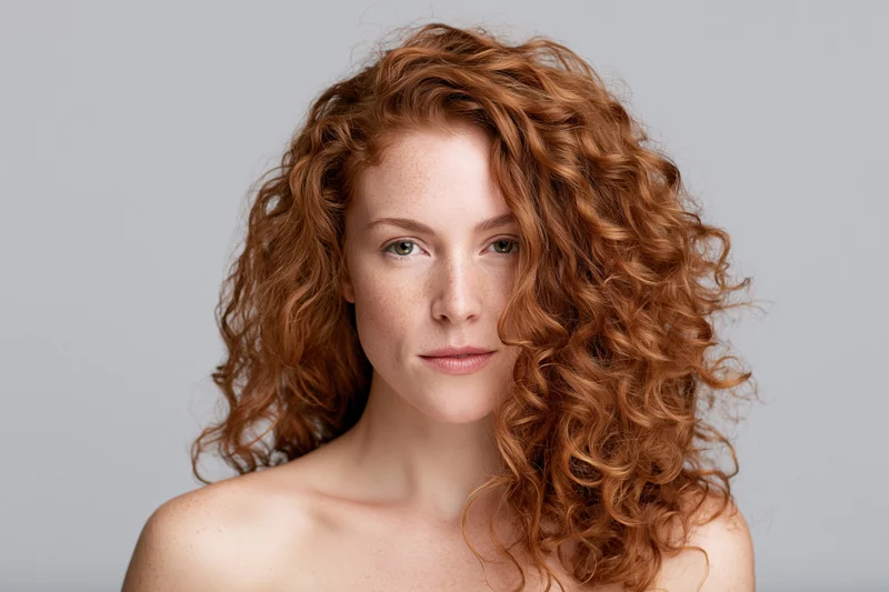 Woman with voluminous auburn curly hair in studio portrait