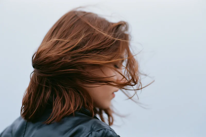 Woman with auburn hair blowing across her face in wind, wearing leather jacket outdoors