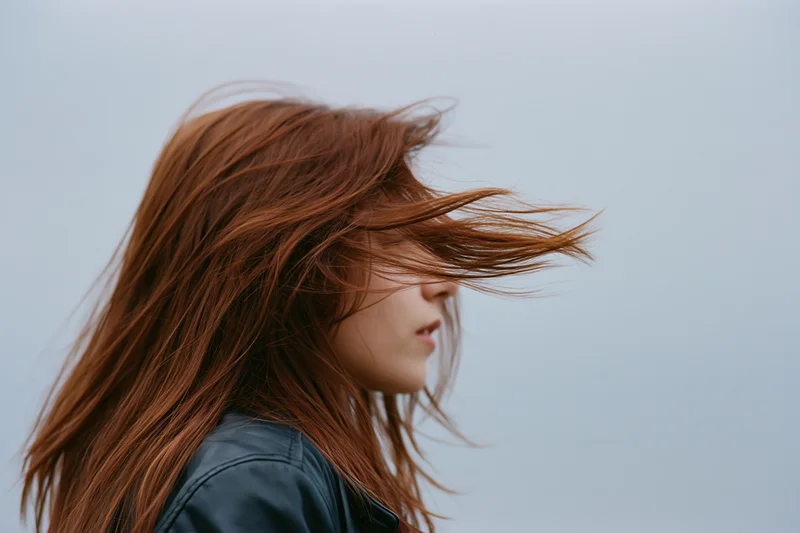 Young woman in profile with auburn hair blowing across her face in the wind outdoors