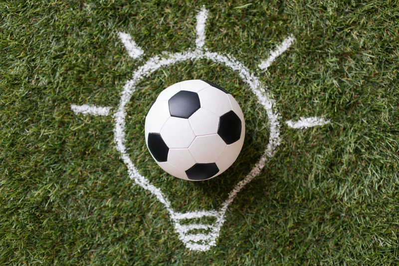 Soccer ball resting on green grass with chalk-drawn lightbulb outline around it