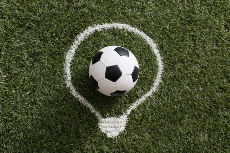 Soccer ball resting on green grass within a white chalk lightbulb outline