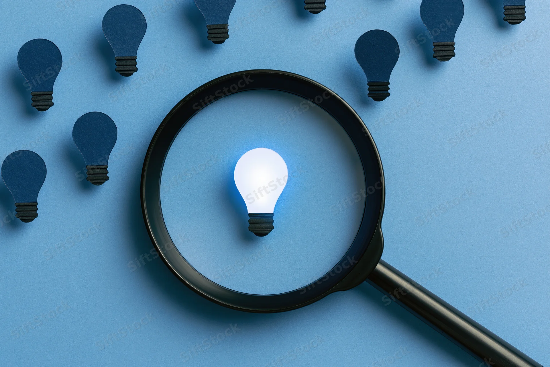 Magnifying glass over a glowing lightbulb on blue paper surface