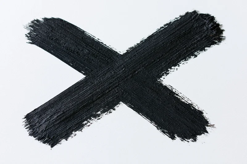 Bold hand-painted black x mark on white background made with dry brush strokes