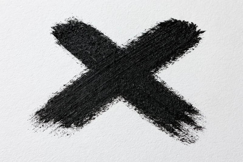 Bold hand-painted black x mark on textured white paper