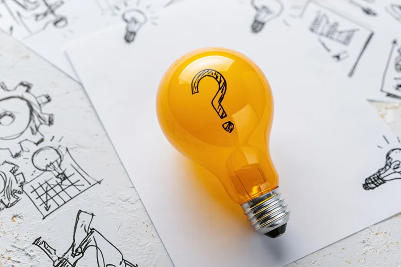 Yellow lightbulb with question mark resting on papers with hand-drawn sketches of ideas and diagrams