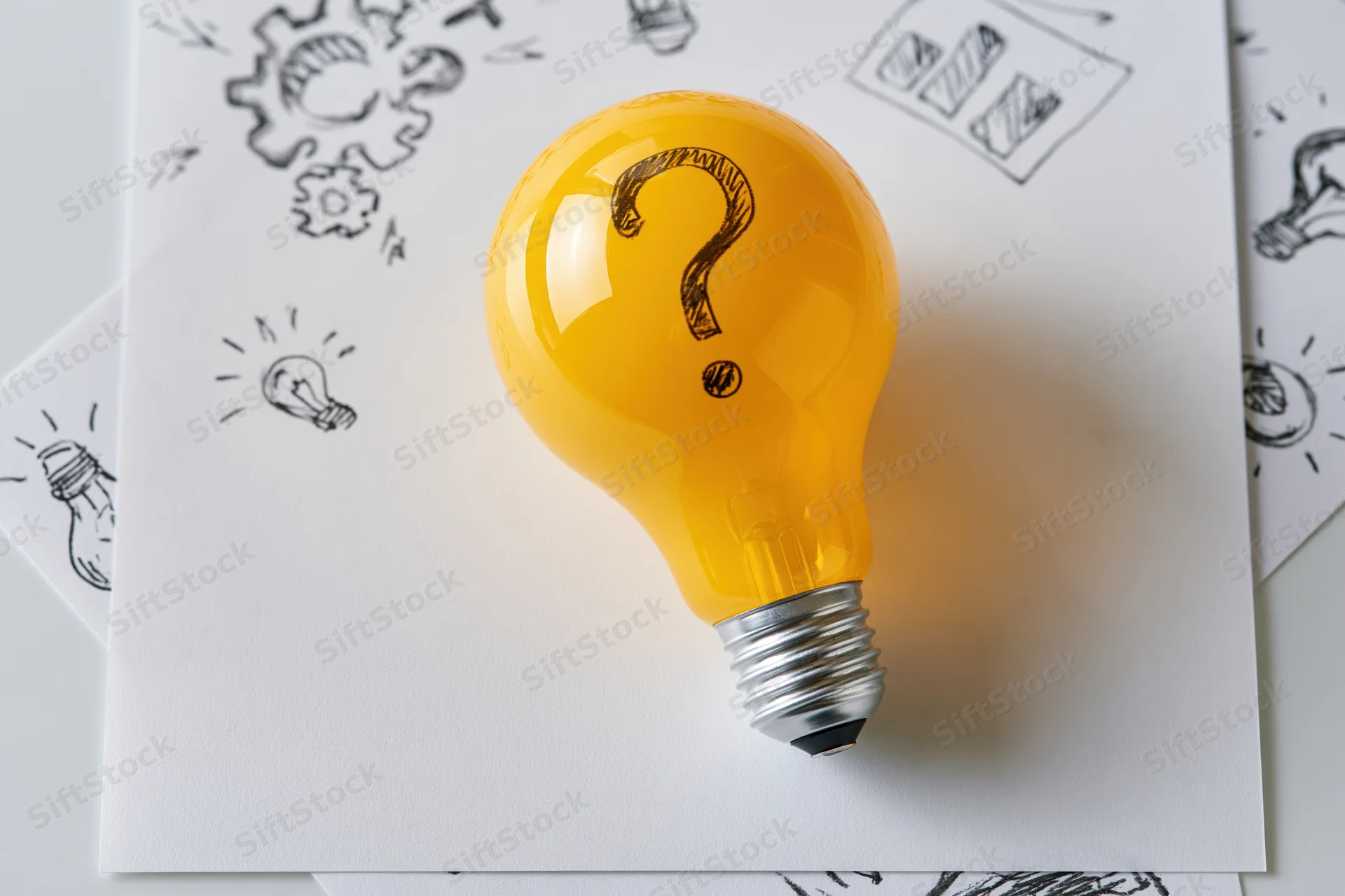 Yellow lightbulb with question mark on paper surrounded by sketches of ideas