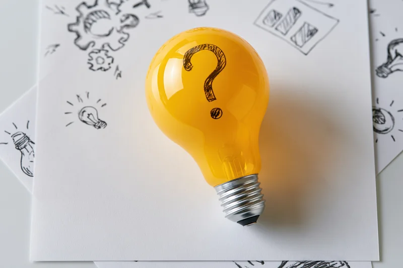 Yellow lightbulb with question mark on paper surrounded by sketches of ideas