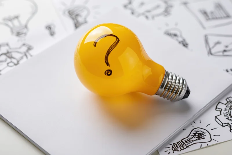 Yellow lightbulb with question mark resting on sketchbook pages filled with idea drawings