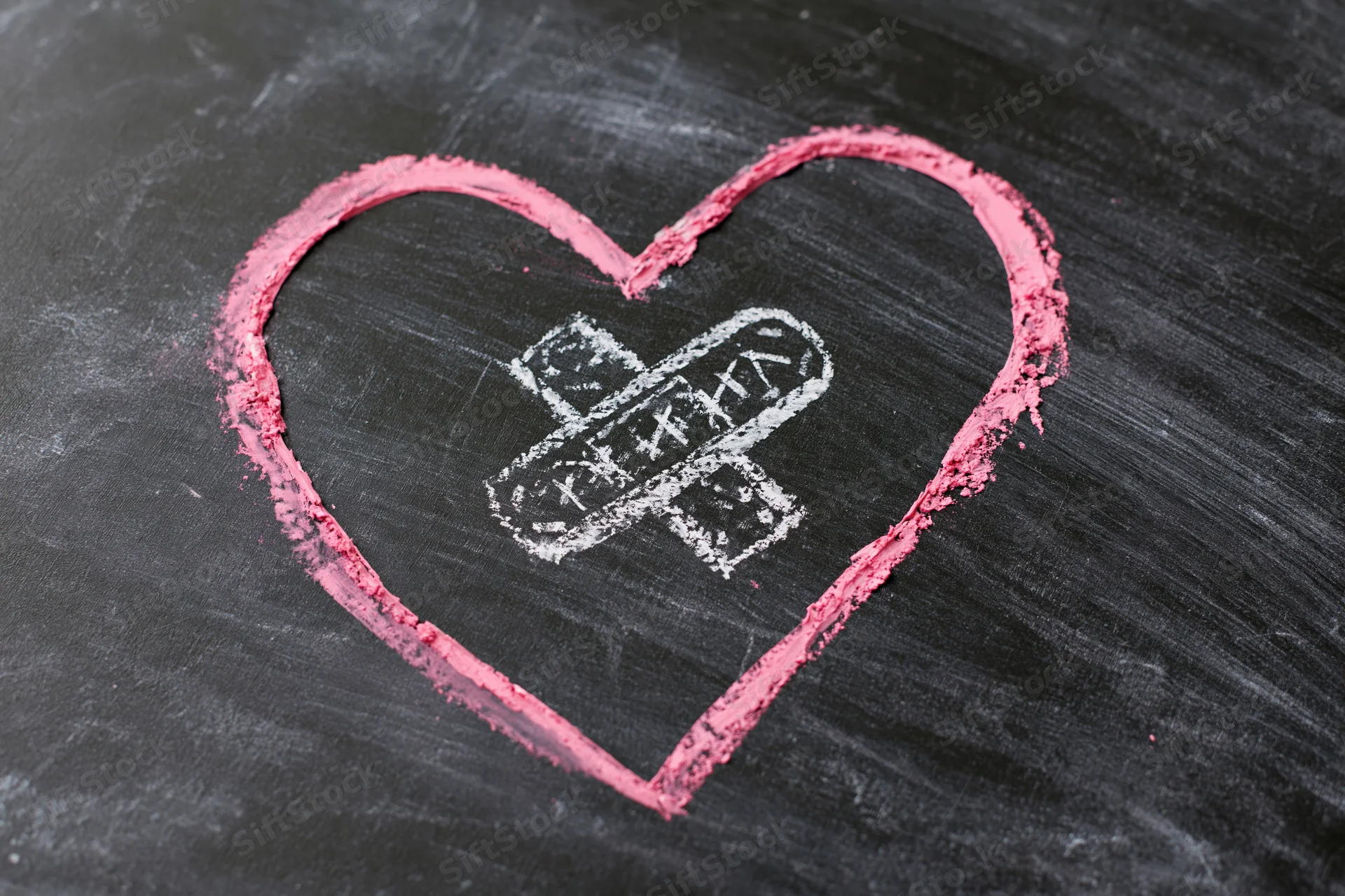Pink chalk heart with white bandage drawn on blackboard surface