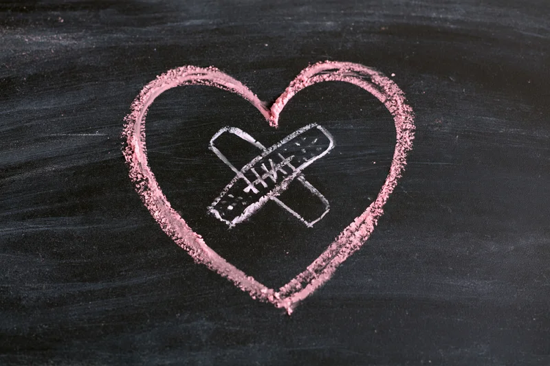 Pink chalk heart with white bandage drawn on blackboard surface