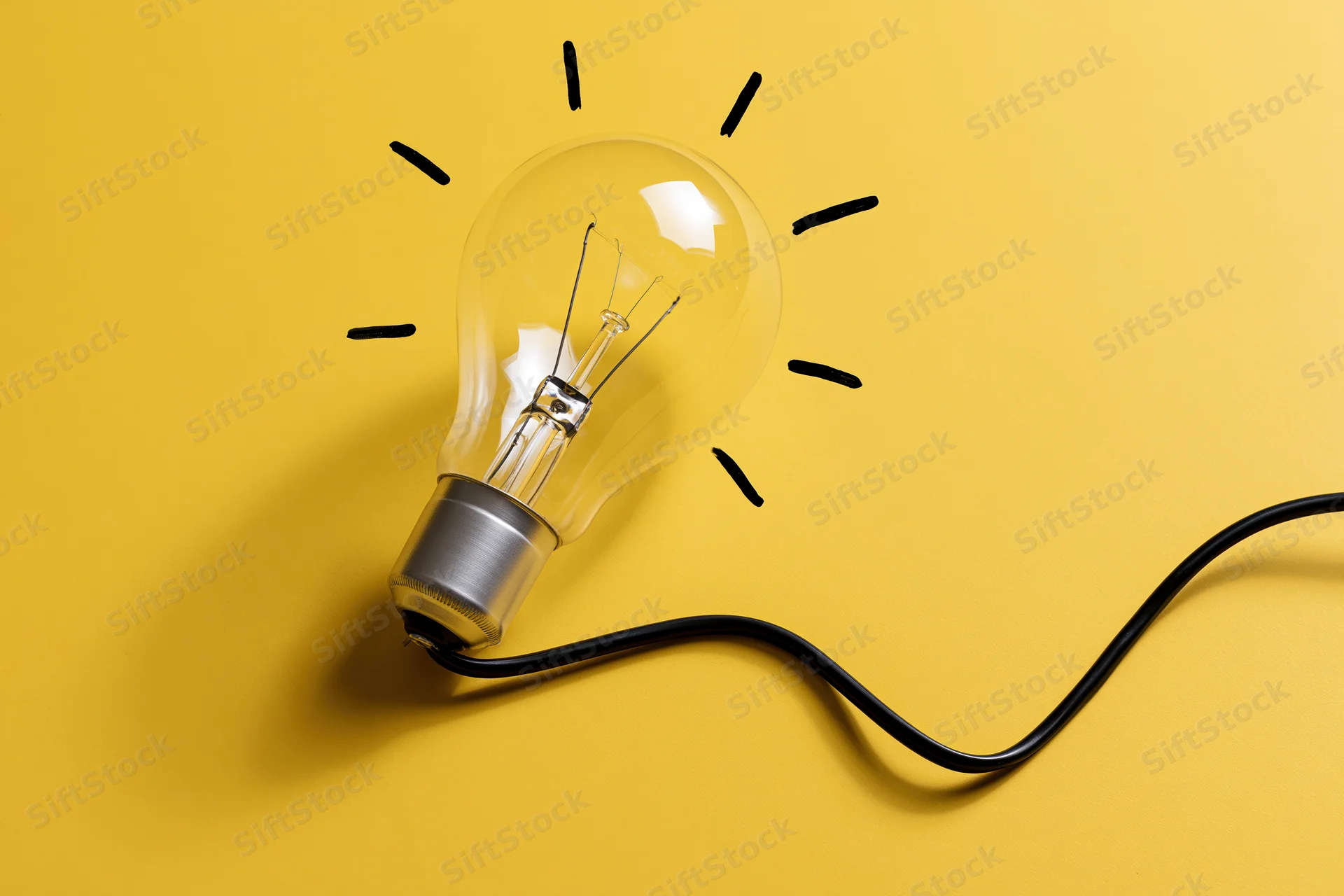 Clear glass incandescent light bulb with drawn rays and black cord on yellow background
