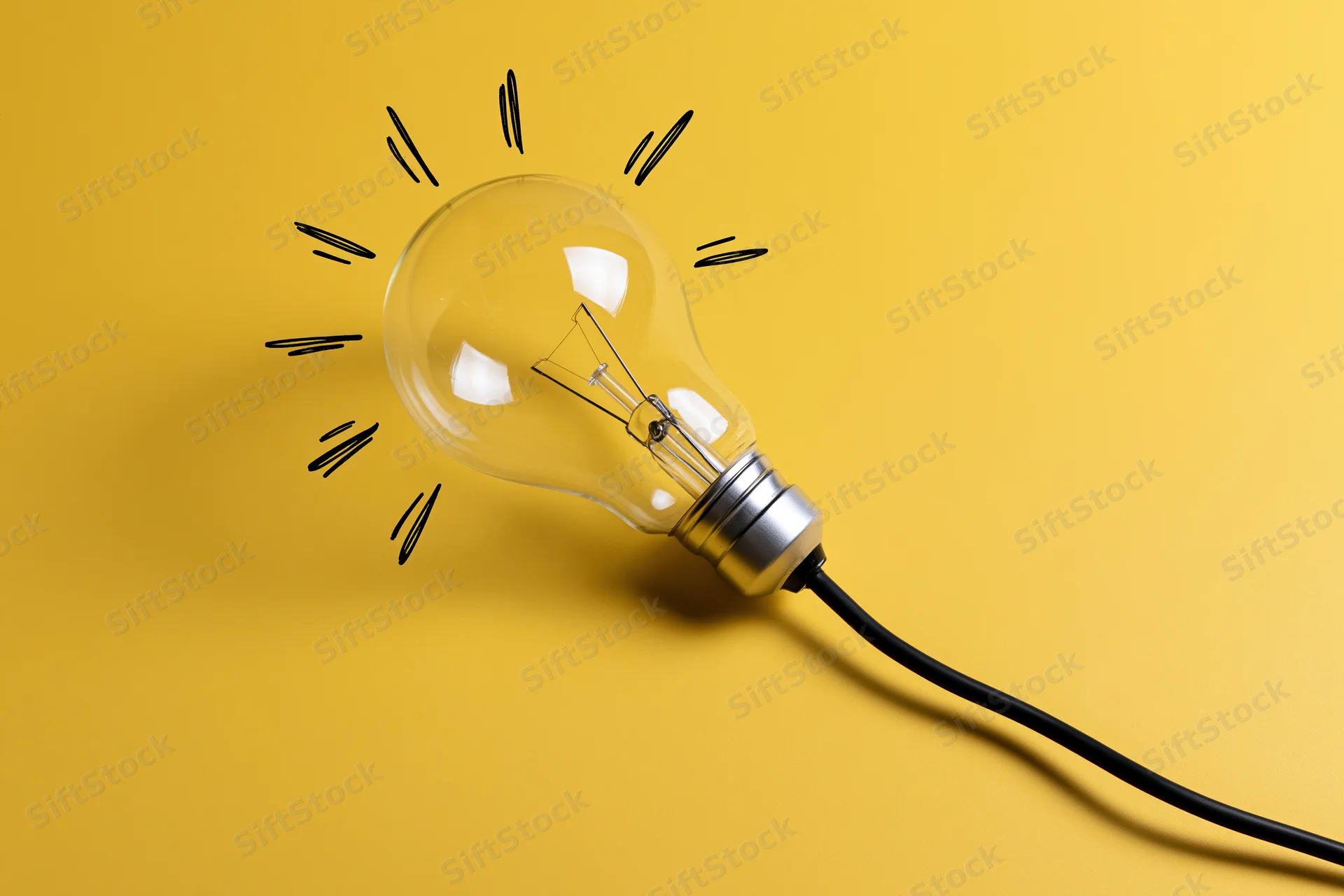 Clear glass incandescent light bulb with hand-drawn rays on yellow background
