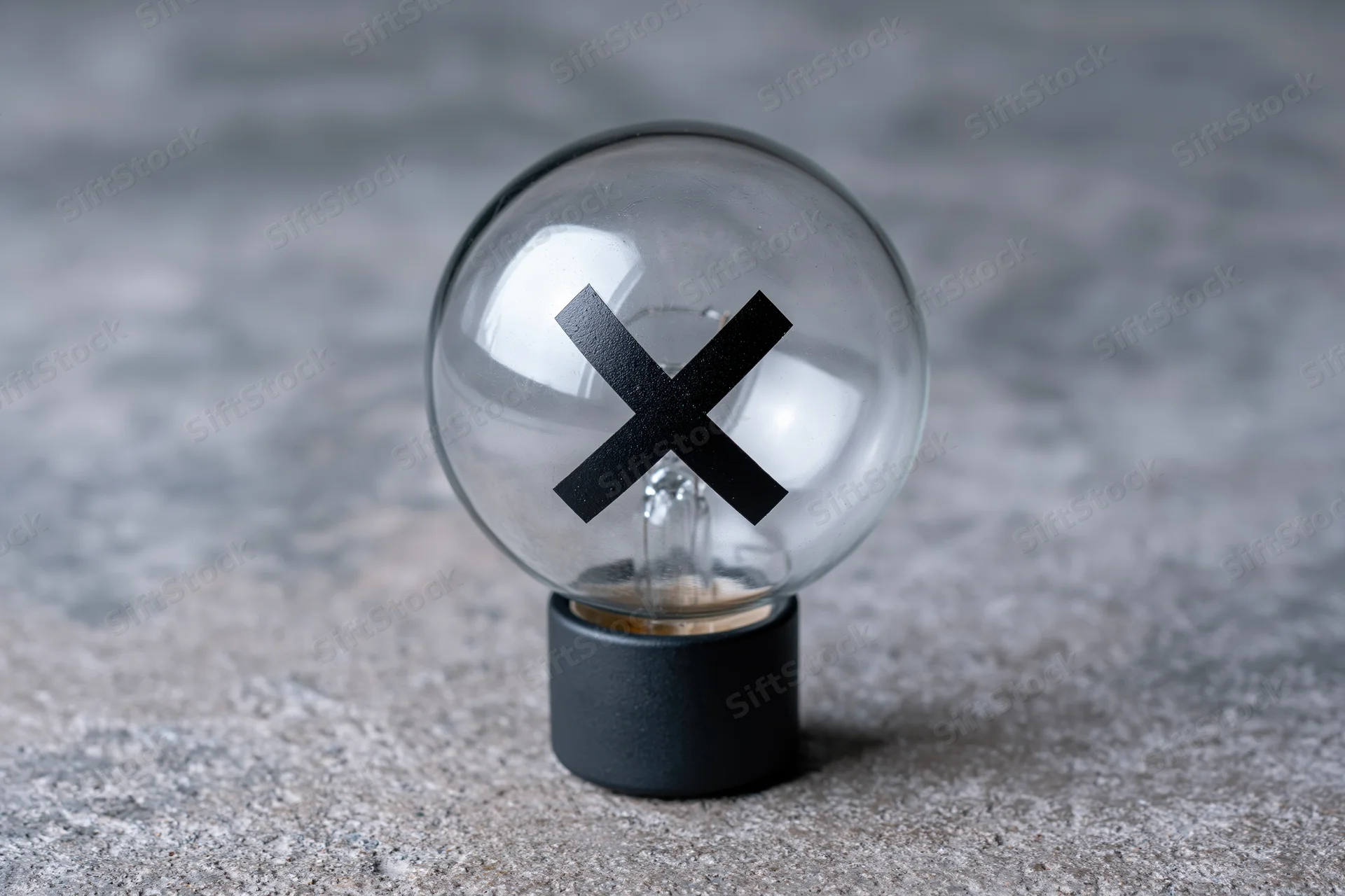 Clear glass light bulb with black x symbol inside on concrete surface