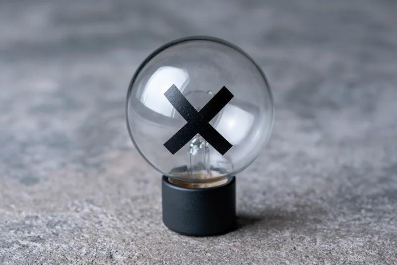 Clear glass light bulb with black x symbol inside on concrete surface