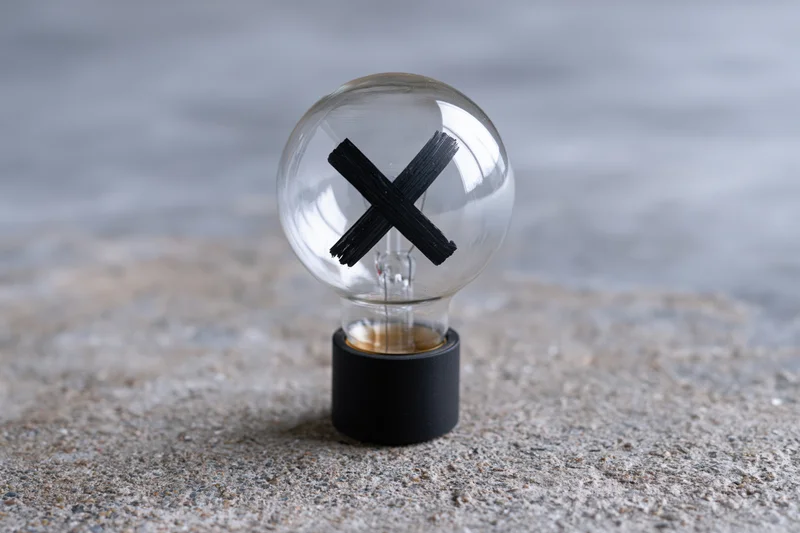 Clear glass light bulb with black x painted inside resting on concrete surface