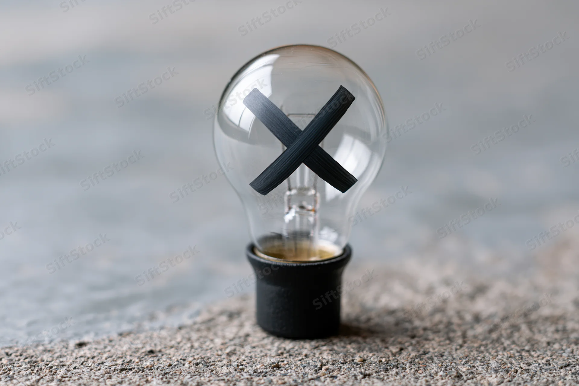 Clear glass light bulb with black x painted inside, resting on textured concrete surface