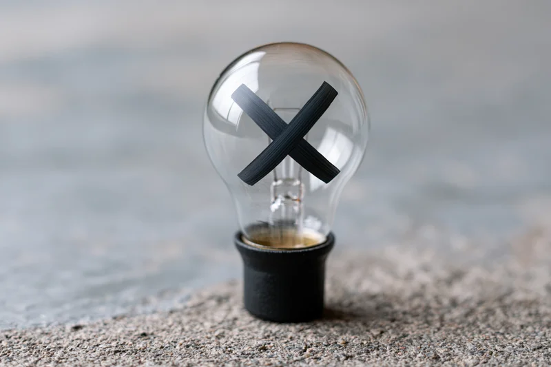 Clear glass light bulb with black x painted inside, resting on textured concrete surface