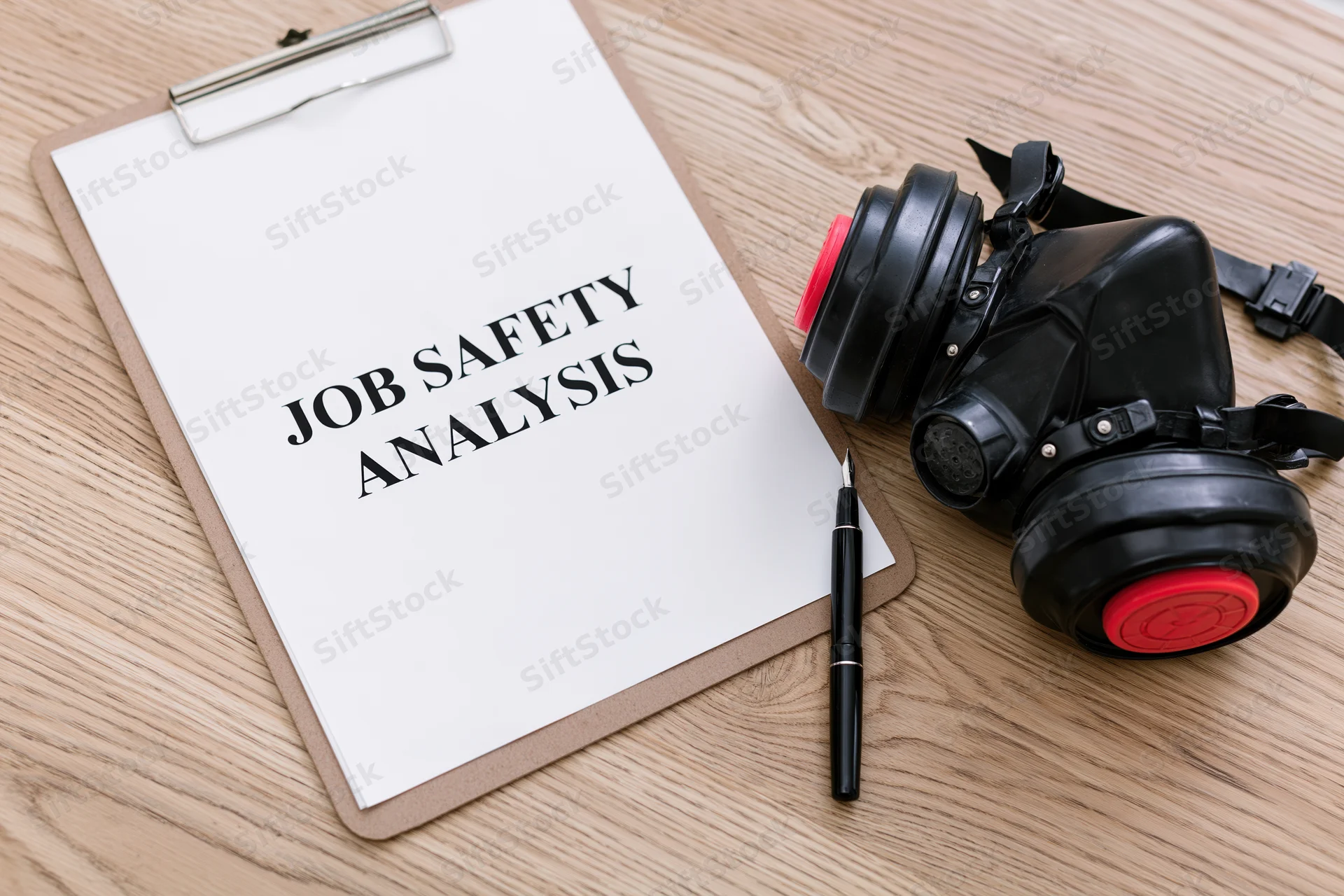 Clipboard with job safety analysis document and respirator mask on wooden desk