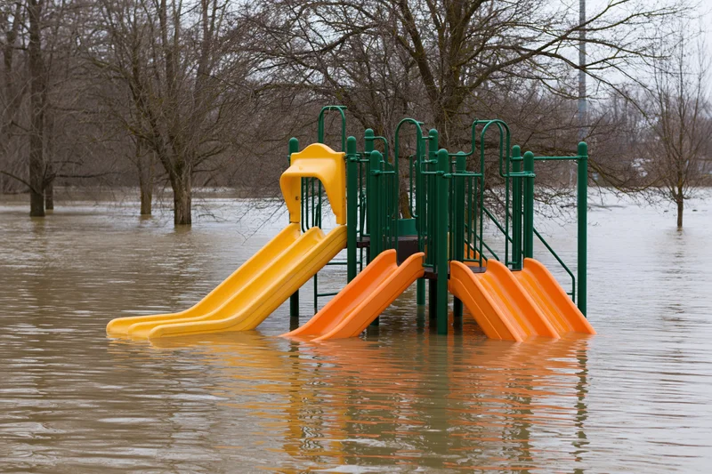 Colorful childrens playground partially submerged in murky floodwater with slides and railings visible above water level
