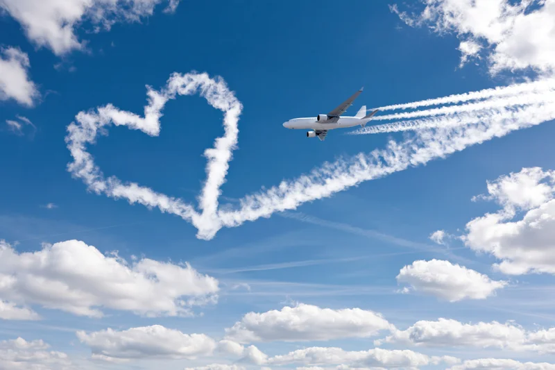 Commercial airplane flying in sky leaving contrail shaped as heart symbol