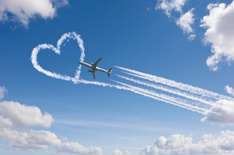 Commercial airplane flying in sky leaving heart-shaped contrail trail
