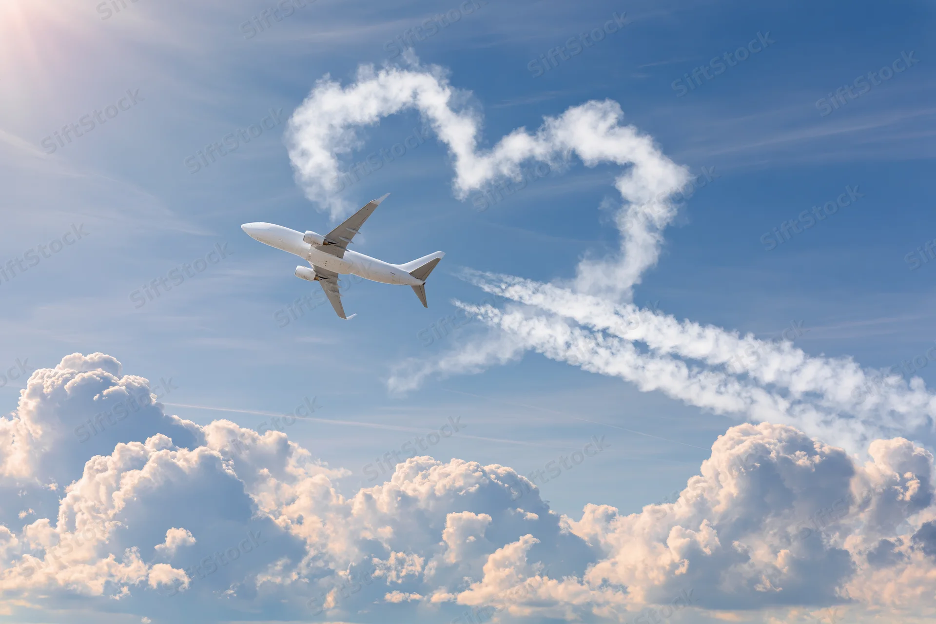 Commercial airplane climbing through sky with heart-shaped cloud formation above fluffy cumulus clouds