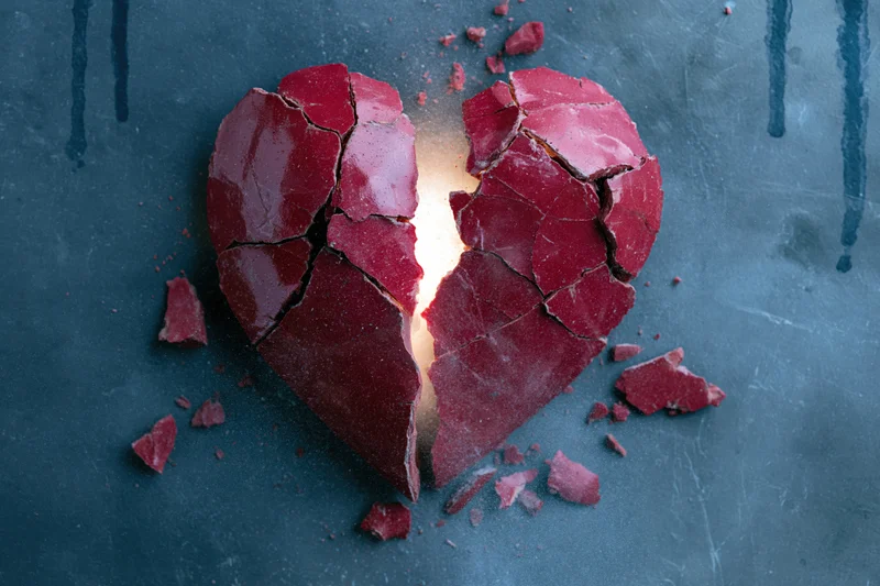 Shattered red ceramic heart with glowing center on dark textured surface