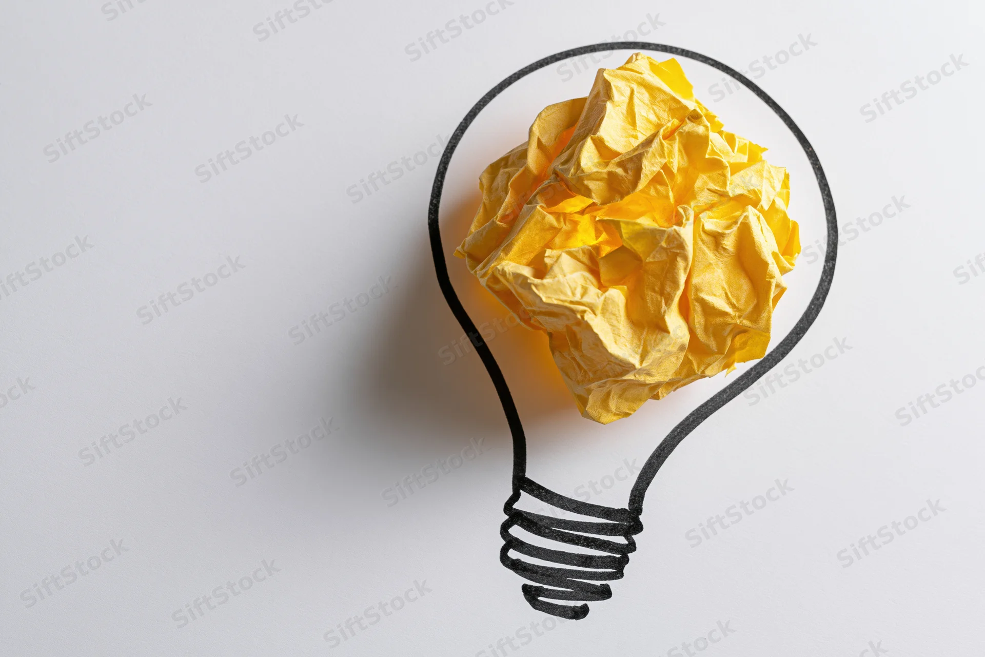 Crumpled yellow paper ball inside hand-drawn lightbulb outline on white surface