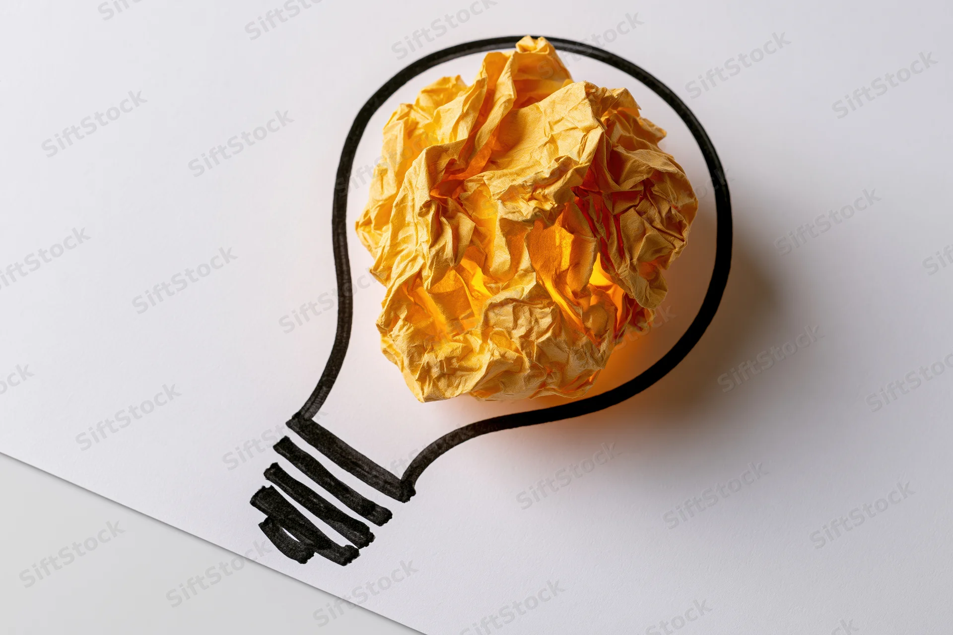 Crumpled yellow paper ball inside hand-drawn lightbulb outline on white paper