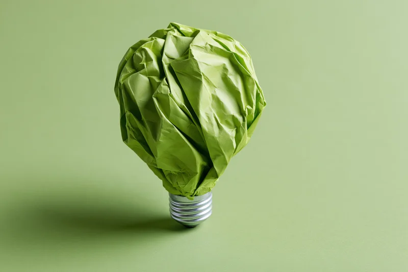 Crumpled green paper shaped as a lightbulb on a green background