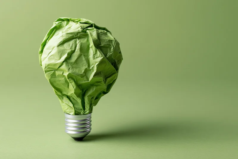 Crumpled green paper shaped as a lightbulb on a green surface