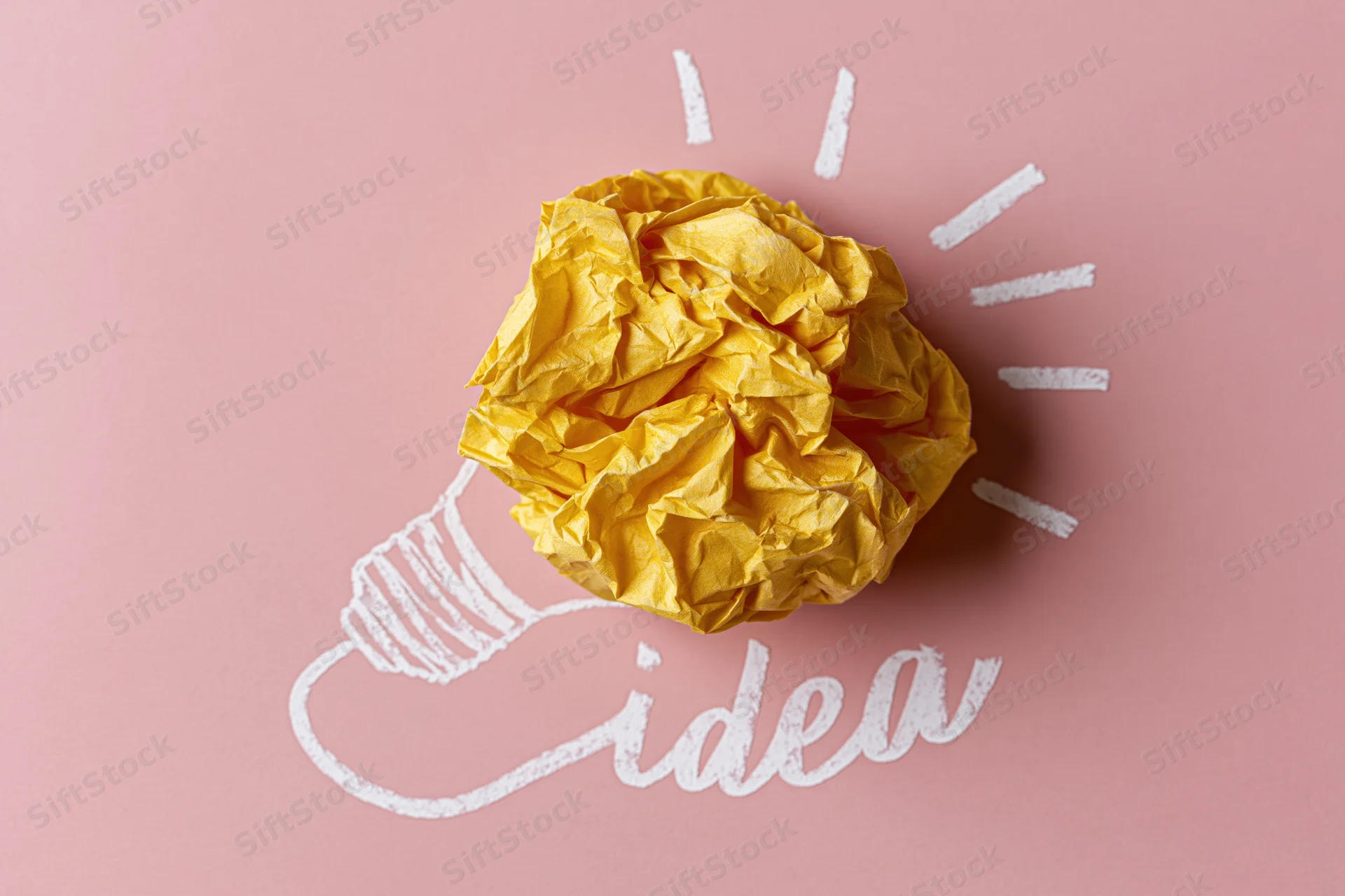 Crumpled yellow paper ball shaped like a light bulb with chalk drawing on pink background