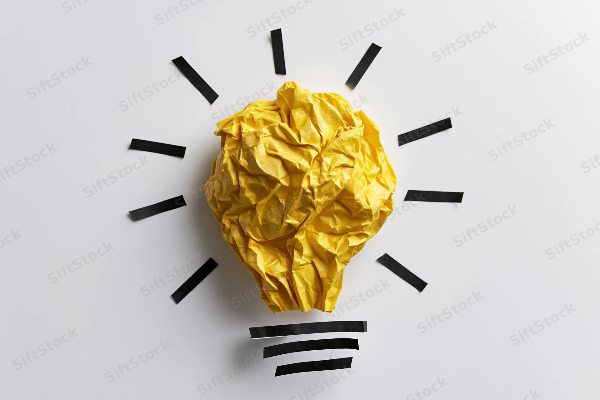 Crumpled yellow paper ball arranged as lightbulb with black rays on white background