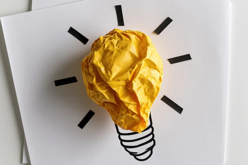 Crumpled yellow paper ball arranged as lightbulb on white paper with black lines radiating from it