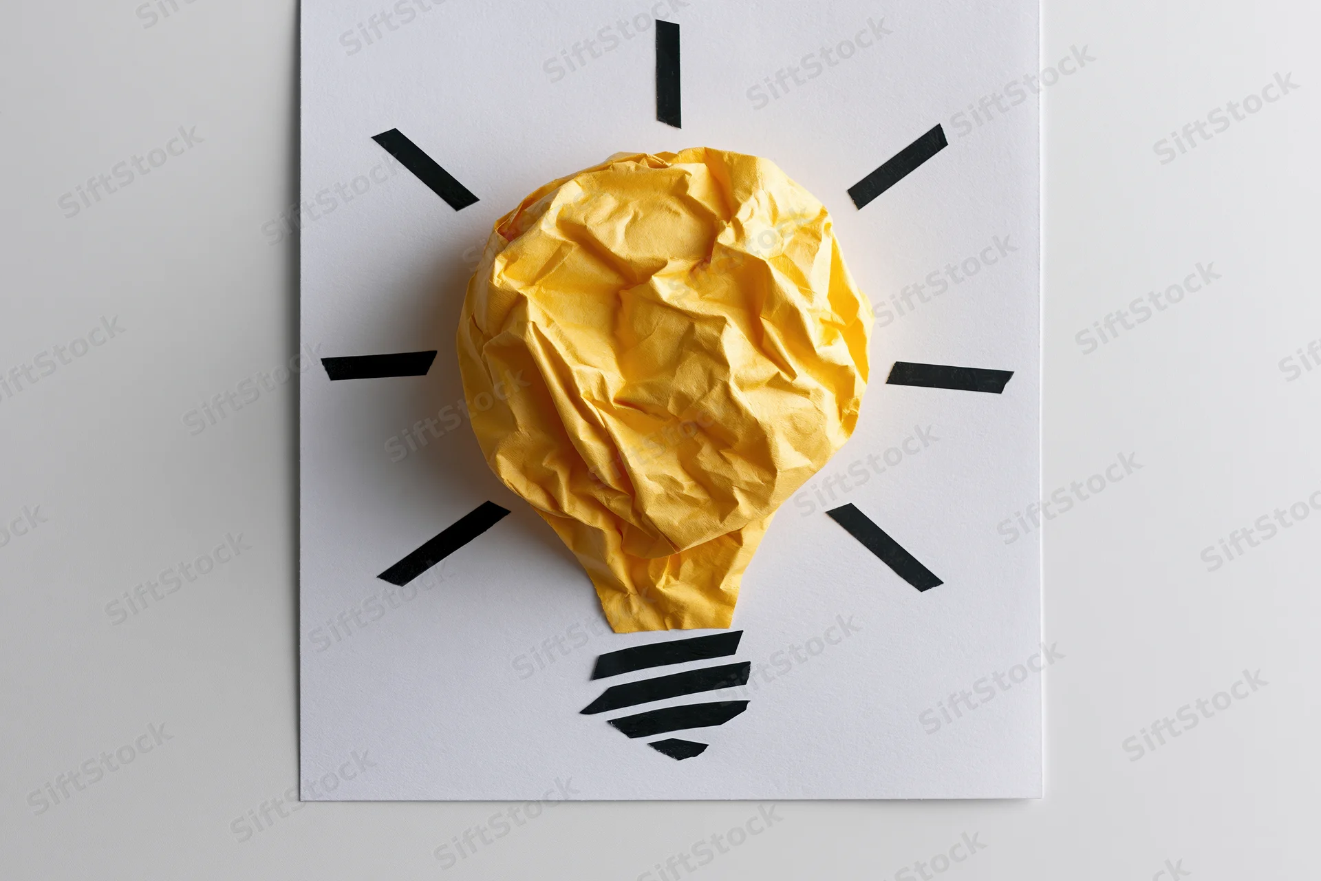Crumpled yellow paper shaped as a lightbulb on white paper with black lines radiating from it