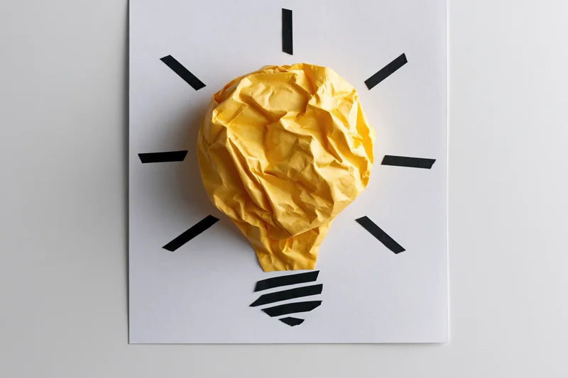 Crumpled yellow paper shaped as a lightbulb on white paper with black lines radiating from it